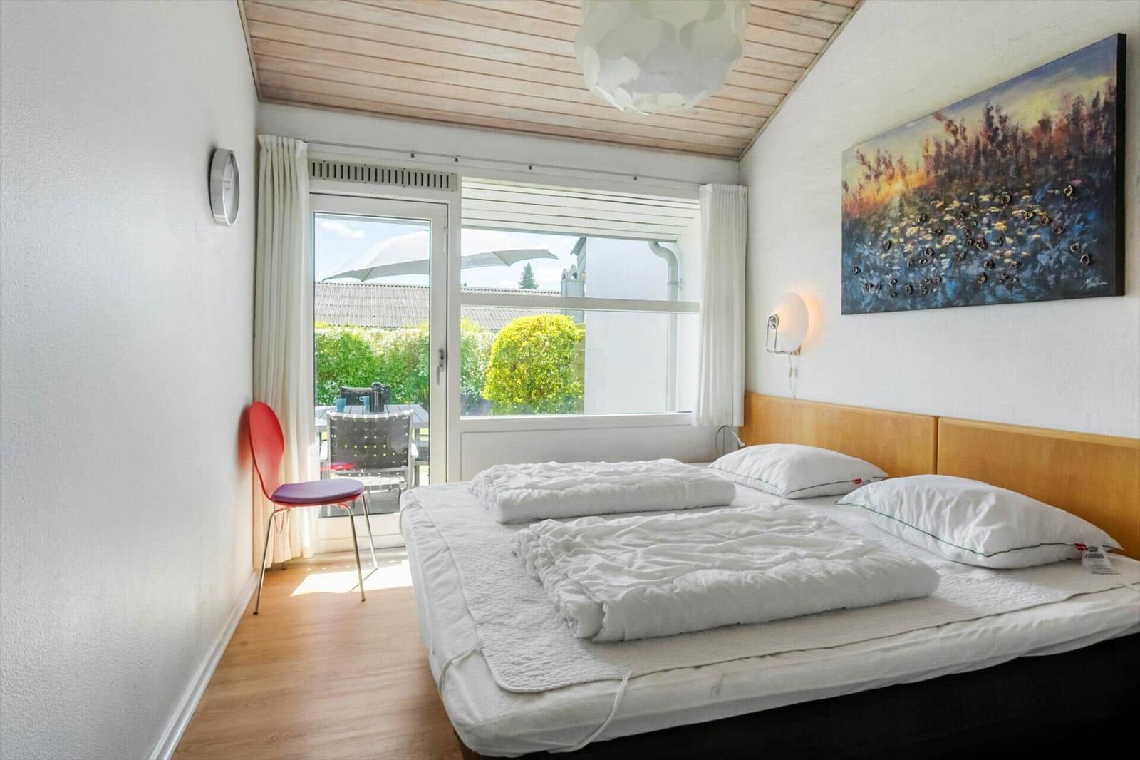 Schlafzimmer mit Bett, Fenster und roter Stuhlecke.