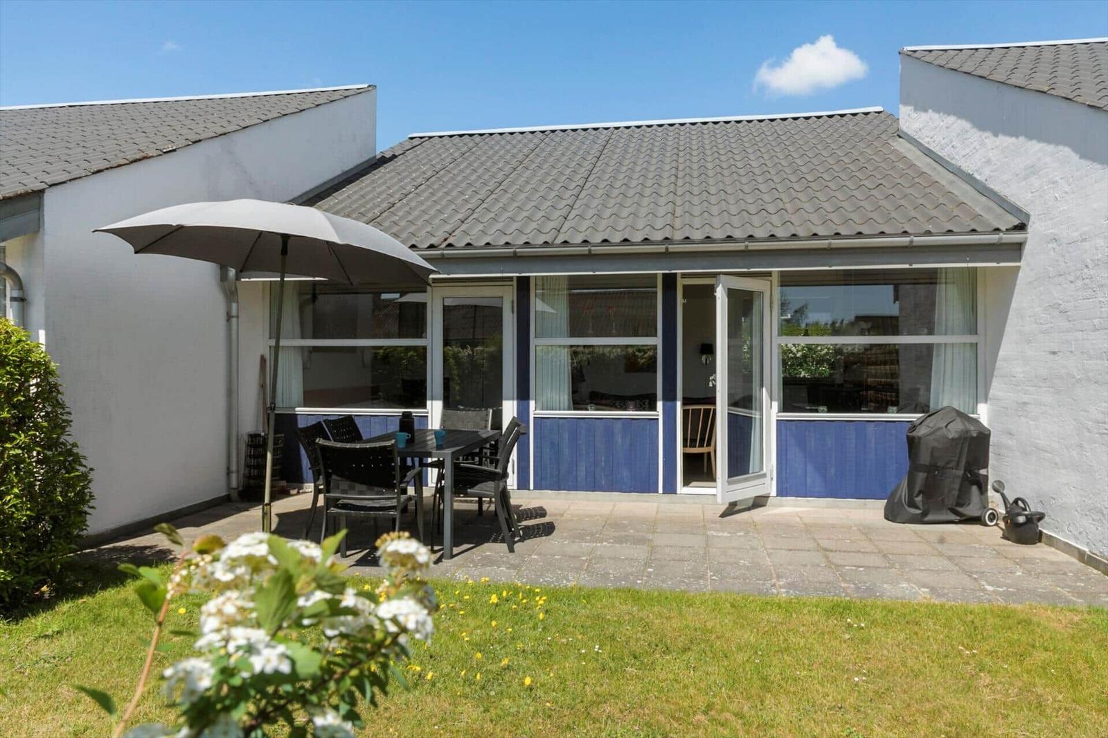 Terrasse mit Tisch, Stühlen und Sonnenschirm. Hinterhof mit Gras und Gartenmöbeln.