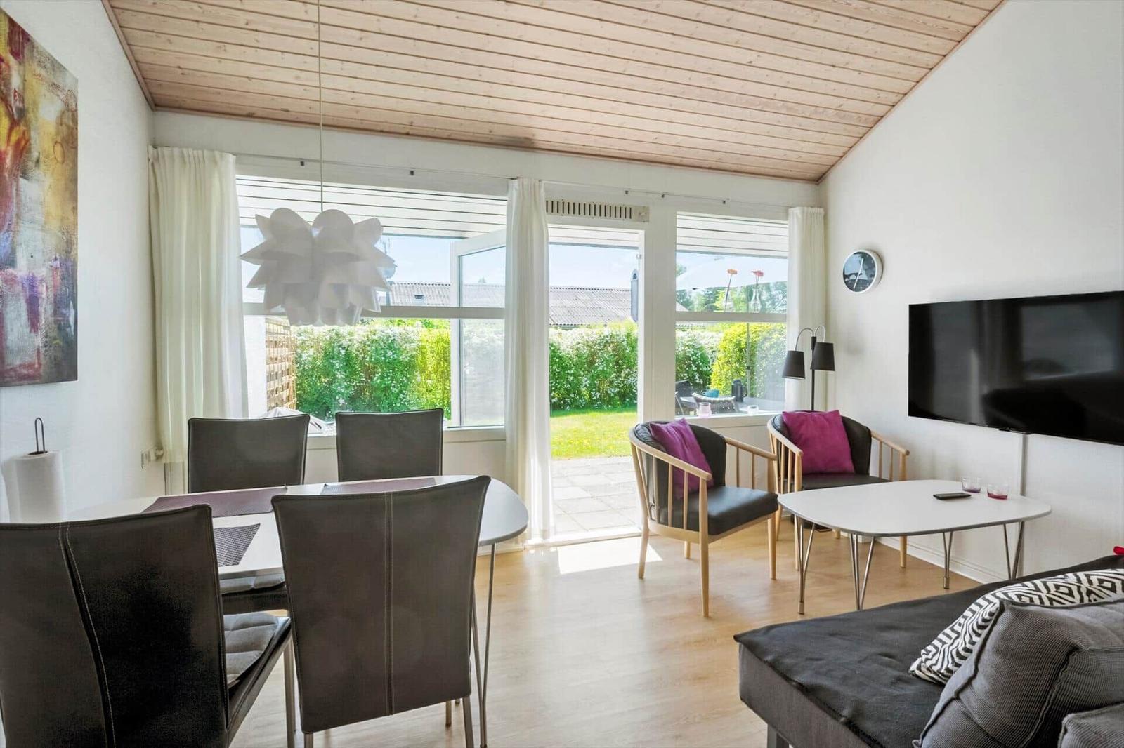Wohn- und Essbereich mit Tisch, Stühlen, Sofa und TV. Durchgang zur Terrasse mit Garten.