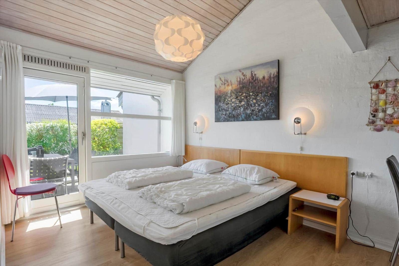 Schlafzimmer mit Doppelbett, Fenster und Balkon. Holzdecke und Wandkunst.