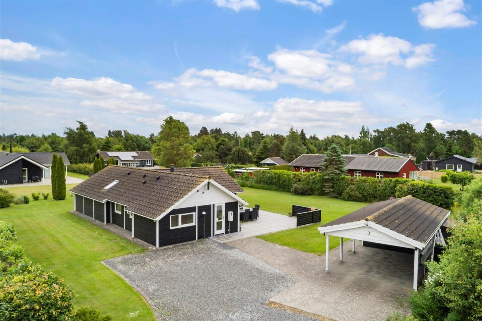 Moderne Ferienhaus mit Terrasse und Carport in grüner Umgebung.