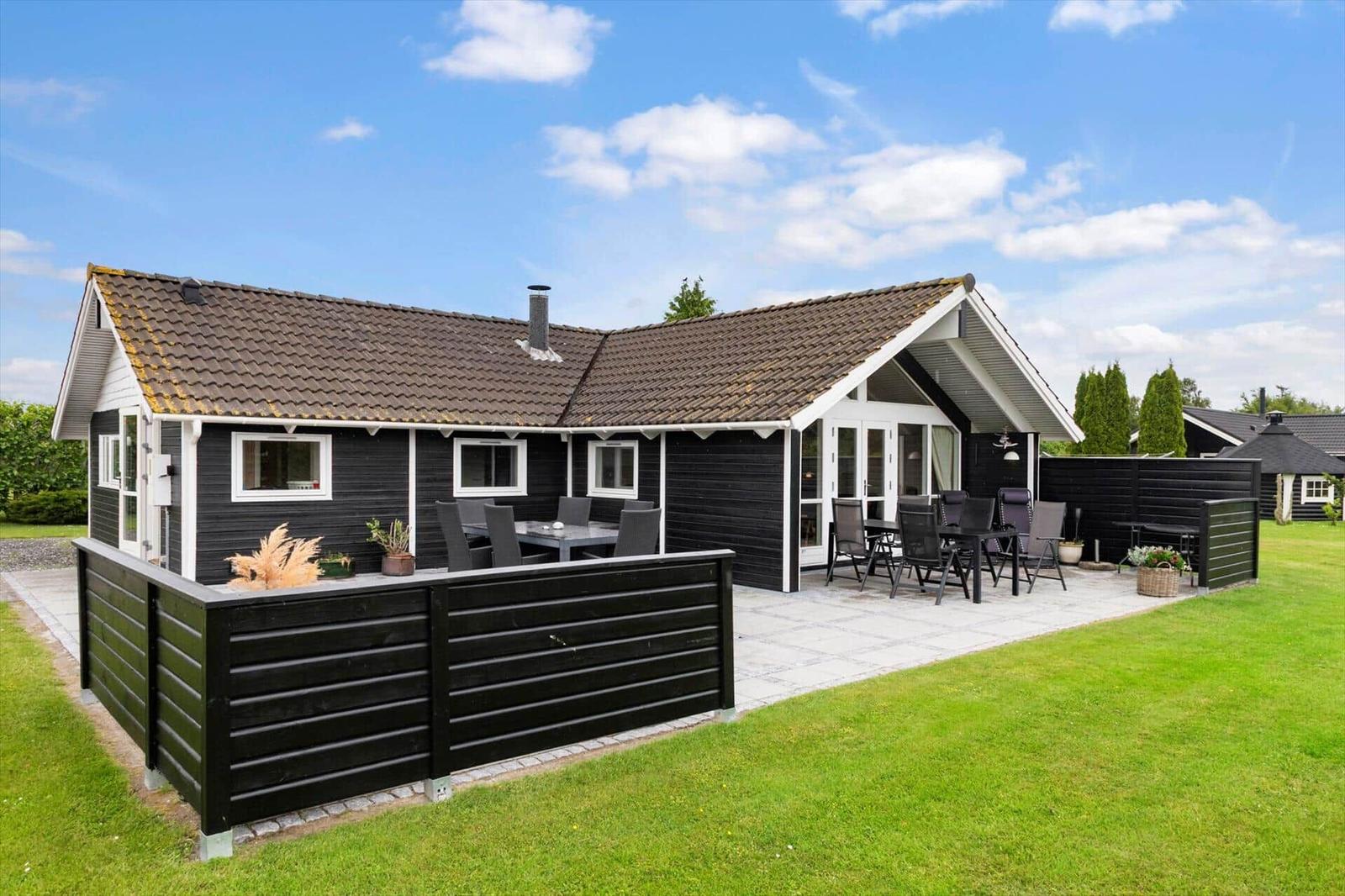 Schwarzes Holzhaus mit Terrasse und Garten. Außentisch und Stühle für Gäste.