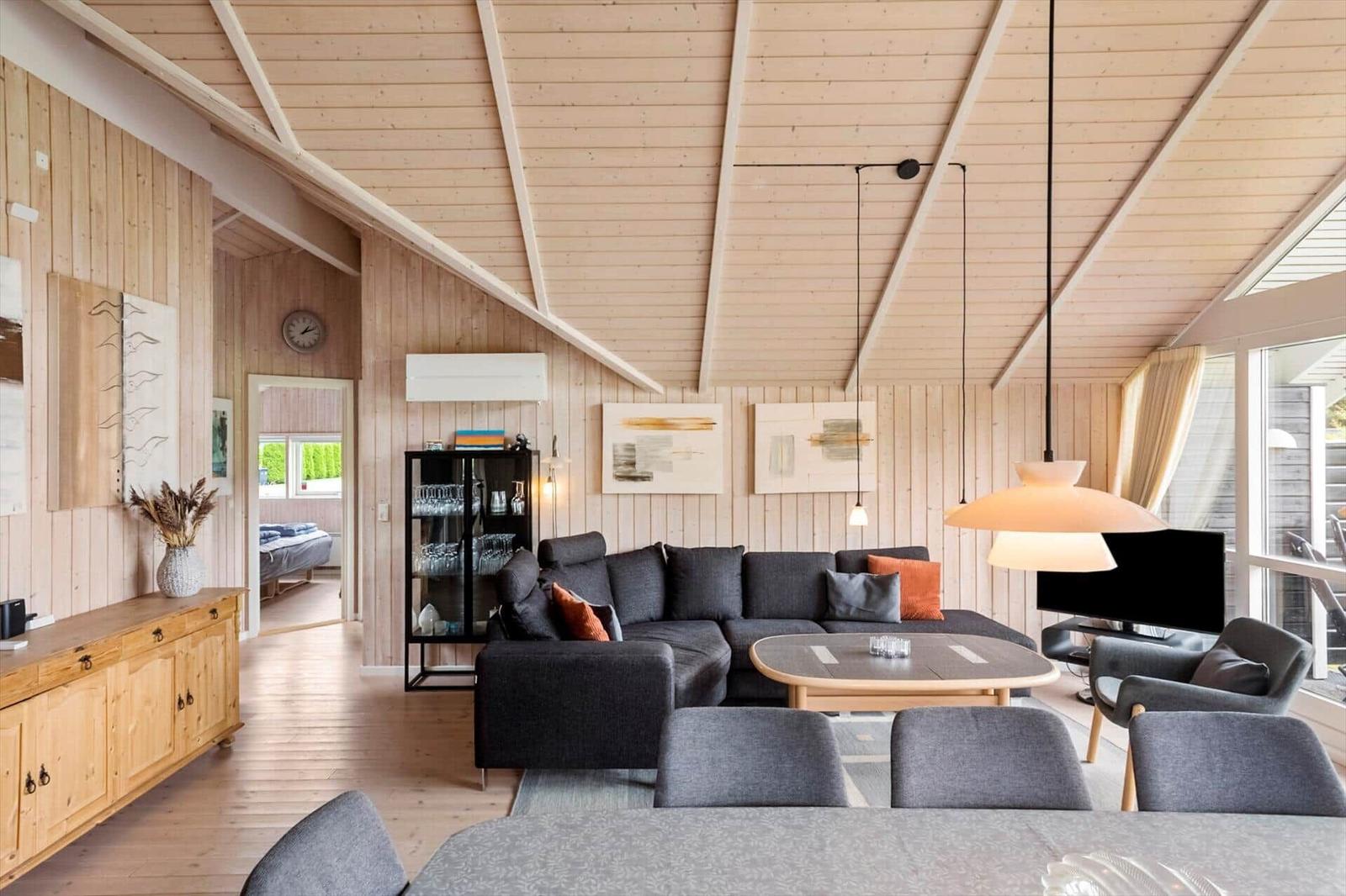 Wohnzimmer mit Sofa, Tisch und Stühlen. Holzwände und Decke. Blick in Schlafzimmer.