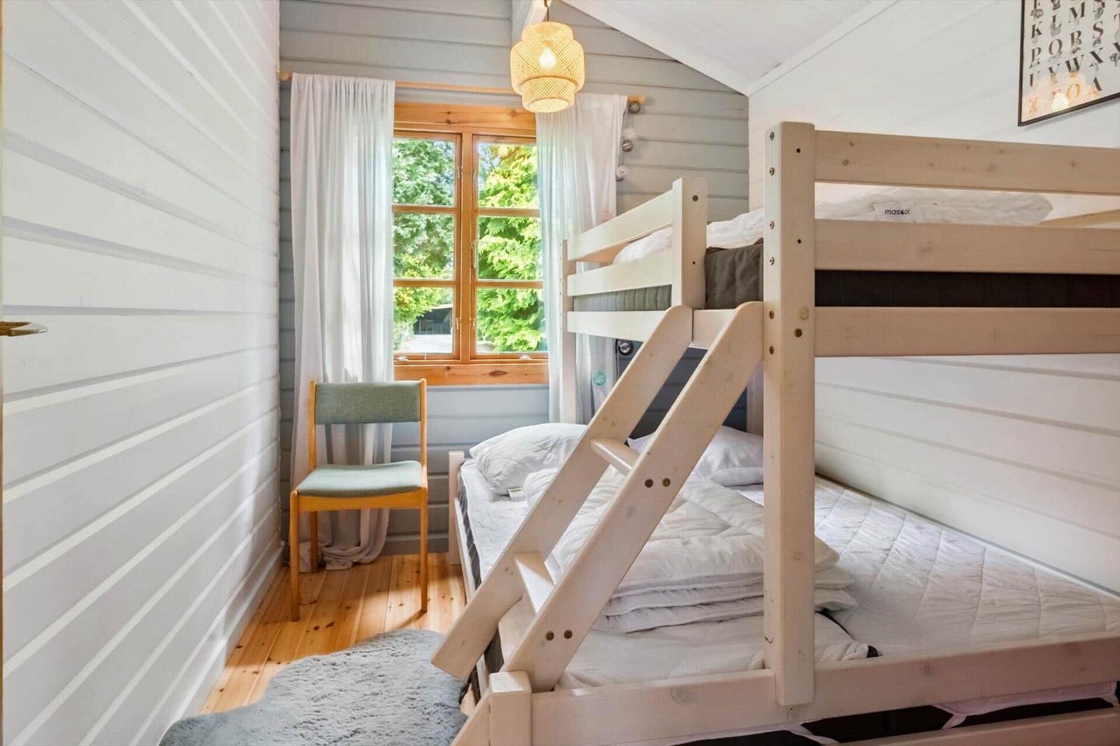 Ein Schlafzimmer mit einem Doppelstockbett, einem Stuhl und einem Fenster mit Blick auf Bäume.