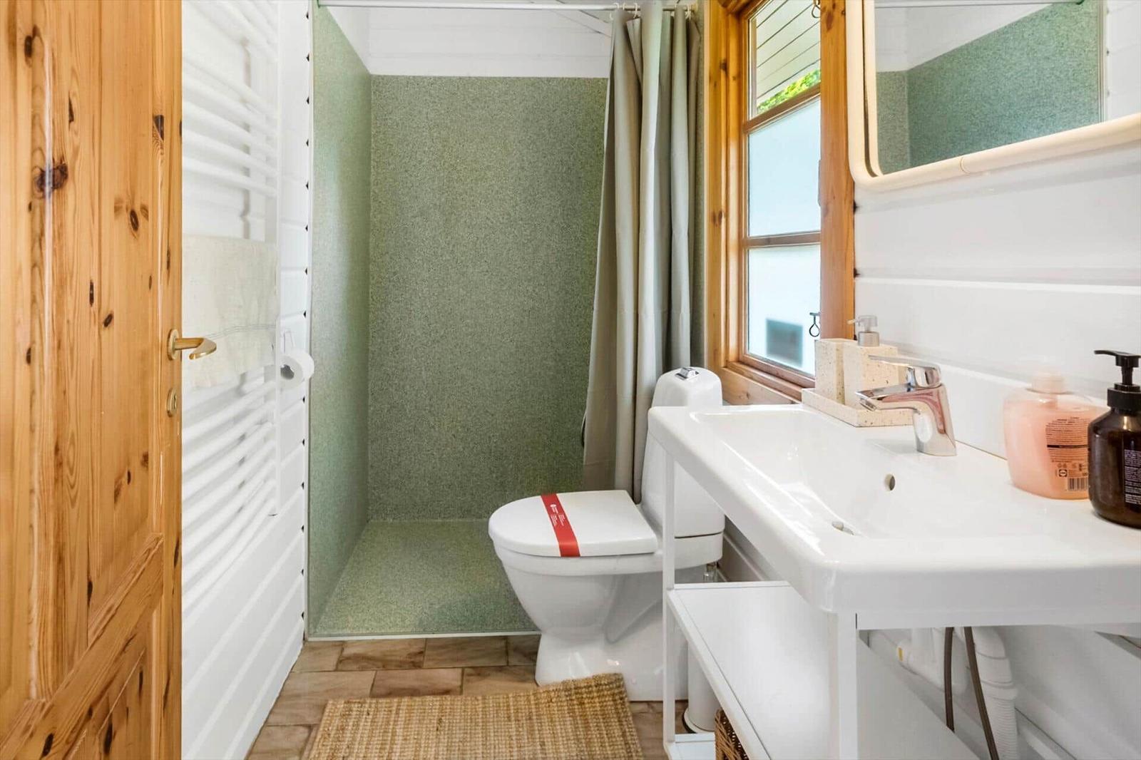 Badezimmer mit Toilette, Waschbecken und Dusche mit grüner Wand.