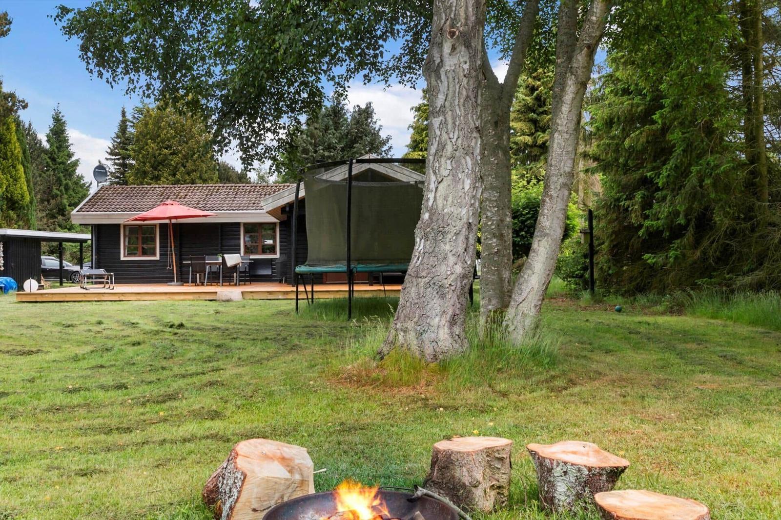 Haus mit Terrasse, Grillplatz und Feuerkorb im Garten. Umgeben von Bäumen und Gras.
