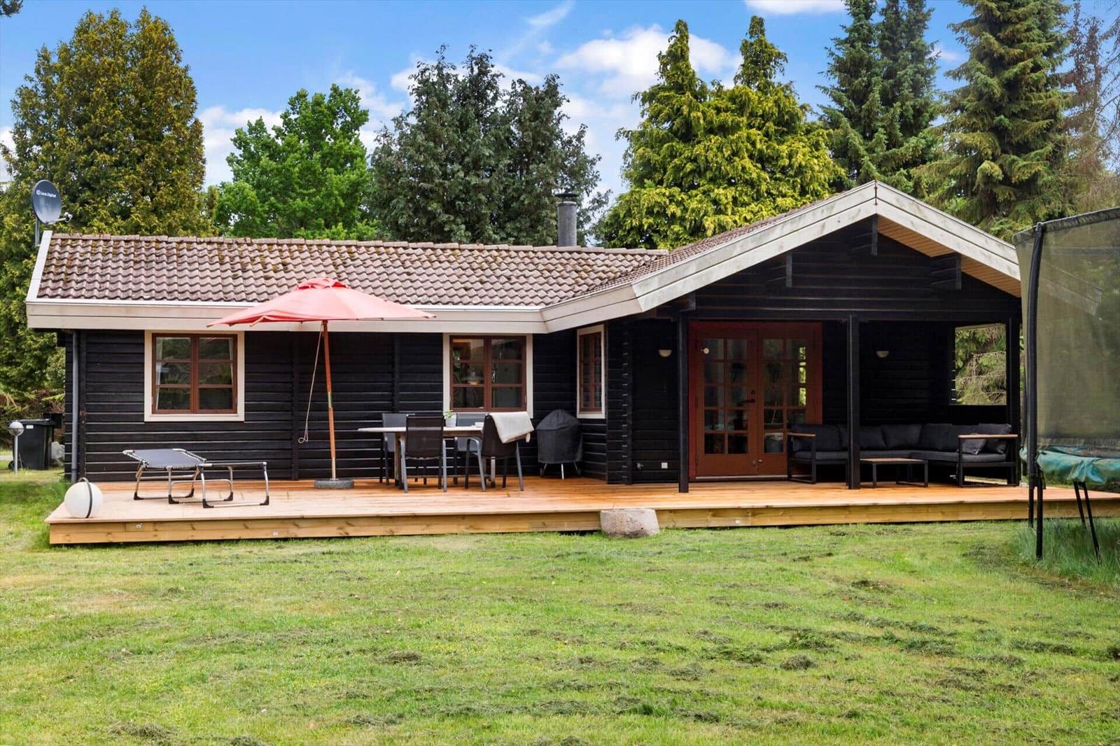 Holzhaus mit Terrasse, Garten und Außensitzgelegenheiten unter Bäumen.