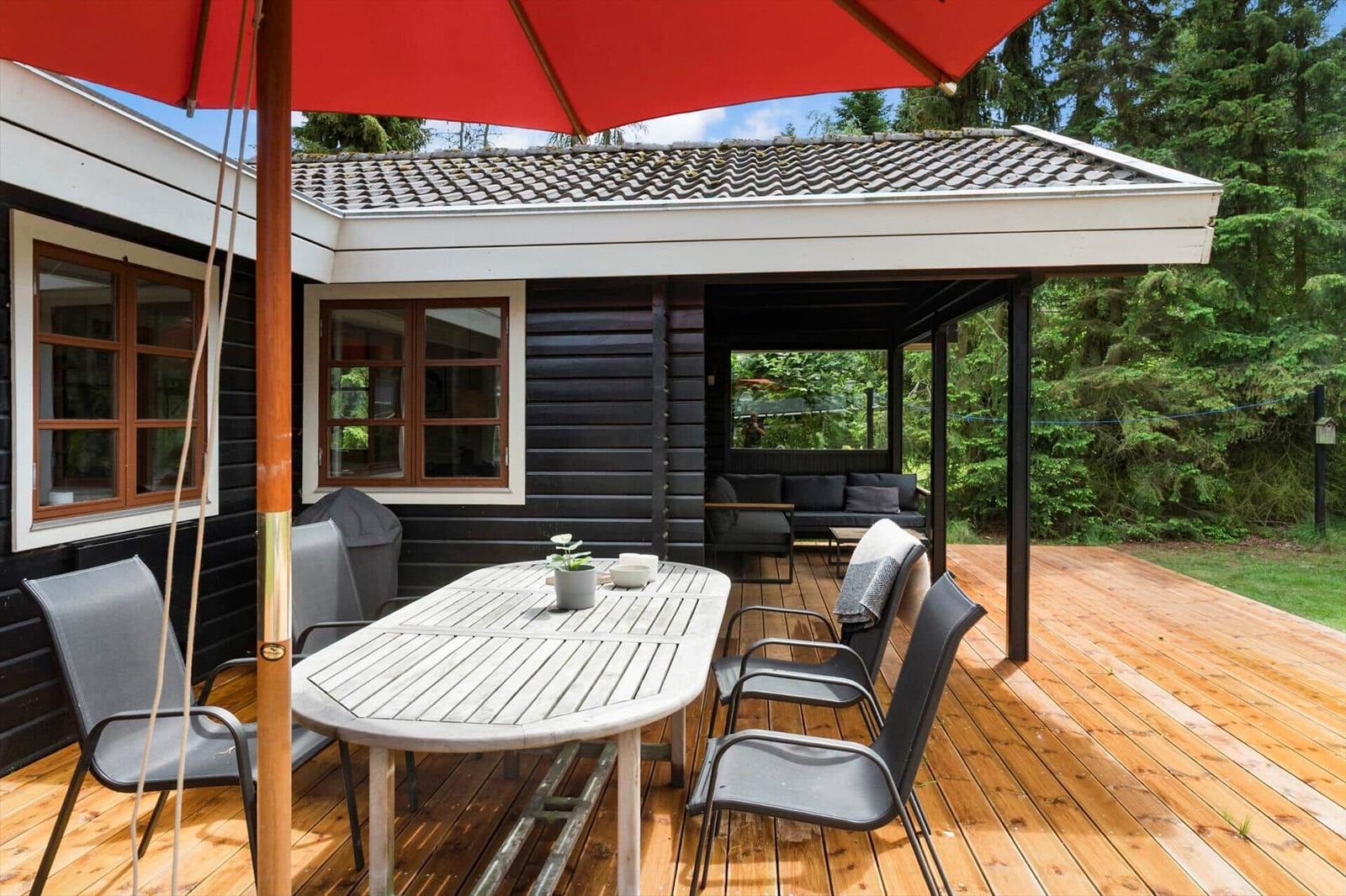 Terrasse mit Tisch, Stühlen und rotem Sonnenschirm vor einem Haus mit Holzfassade.