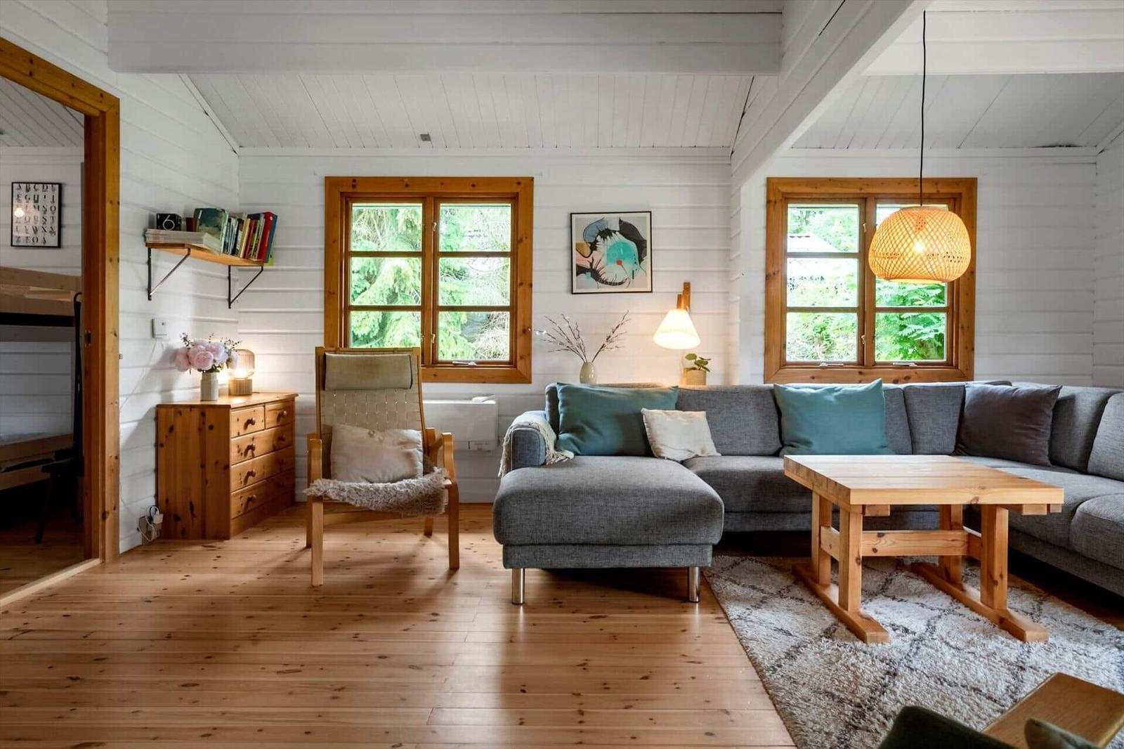 Wohnzimmer mit grauem Sofa, Holztisch und Holzboden. Zwei Fenster und Wandbild.