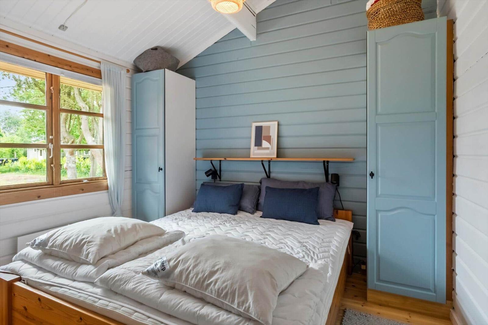 Schlafzimmer mit Bett, blauer Wand und Fenster mit Blick auf Grün.