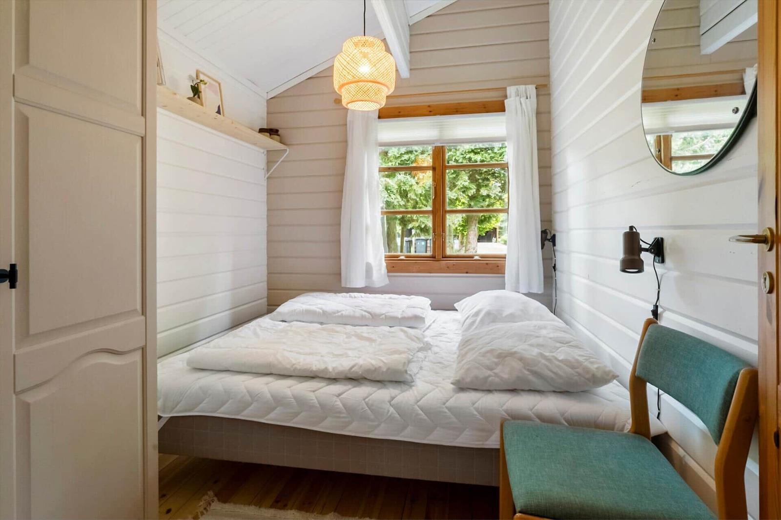 Schlafzimmer mit Bett, Fenster, Stuhl und Deckenleuchte.