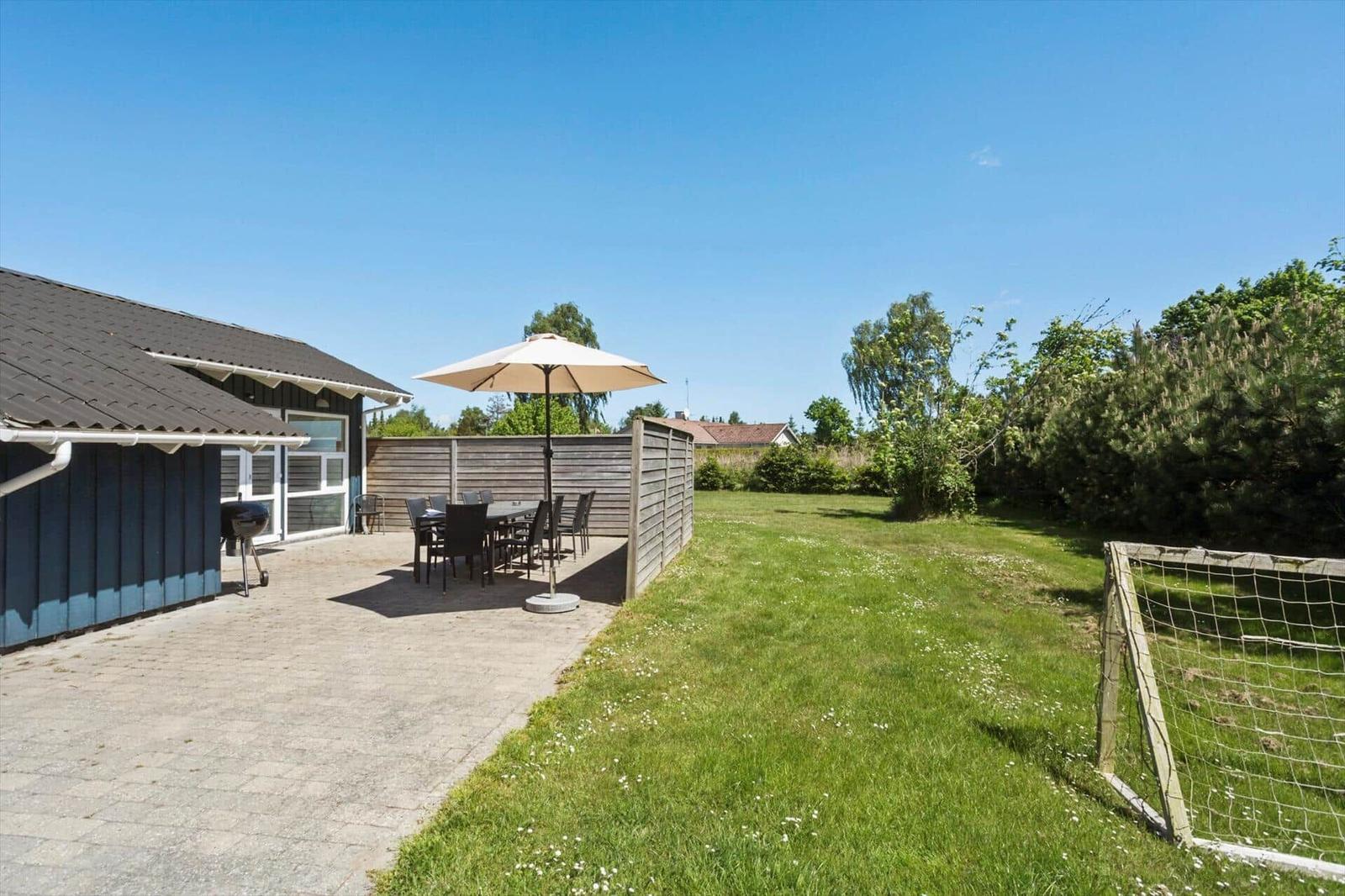 Terrasse mit Tisch, Stühlen und Sonnenschirm neben einem Garten mit Fußballtor.