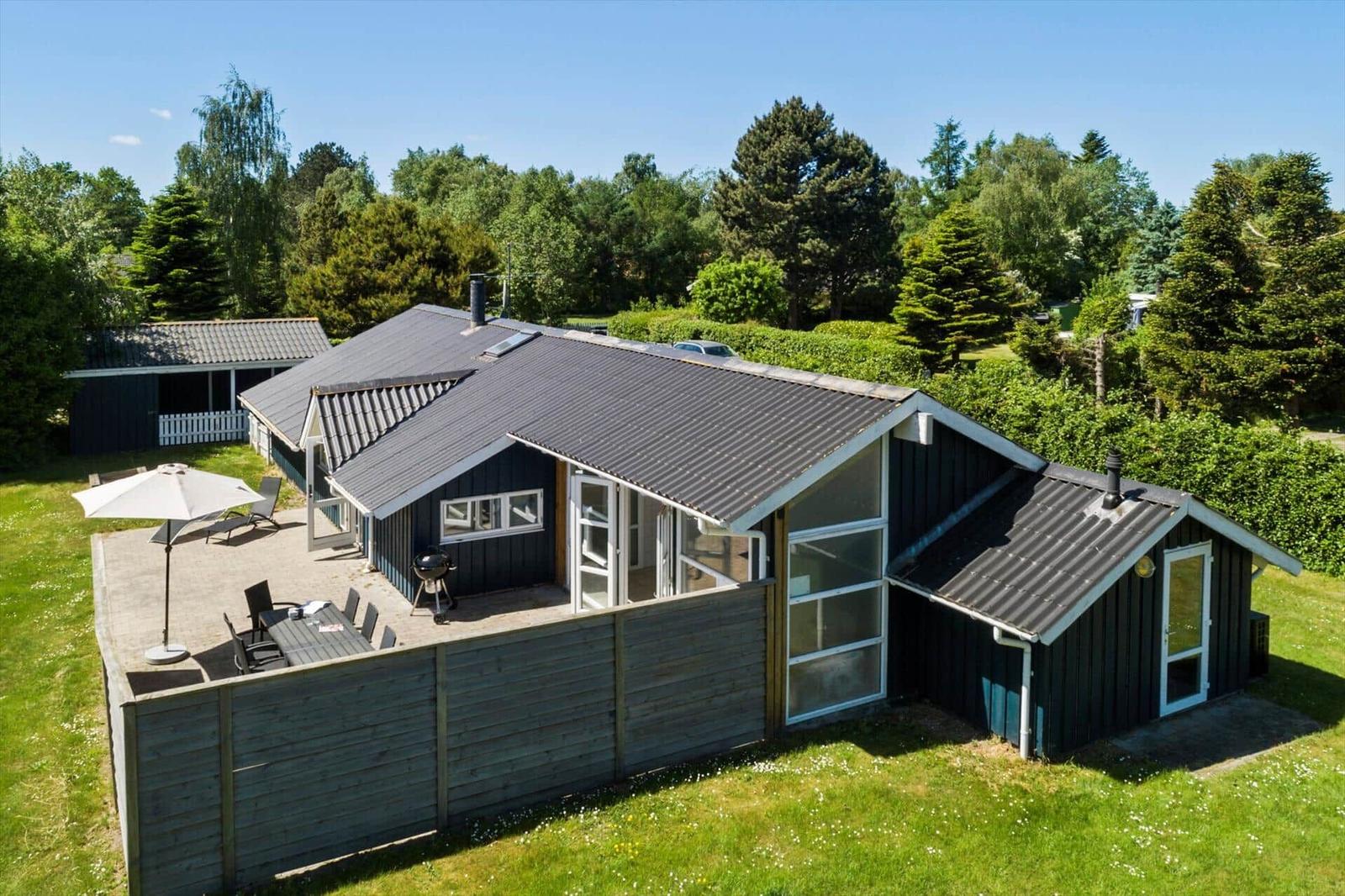 Haus mit Terrasse, Grill und Garten. Umgeben von Bäumen und Gras.