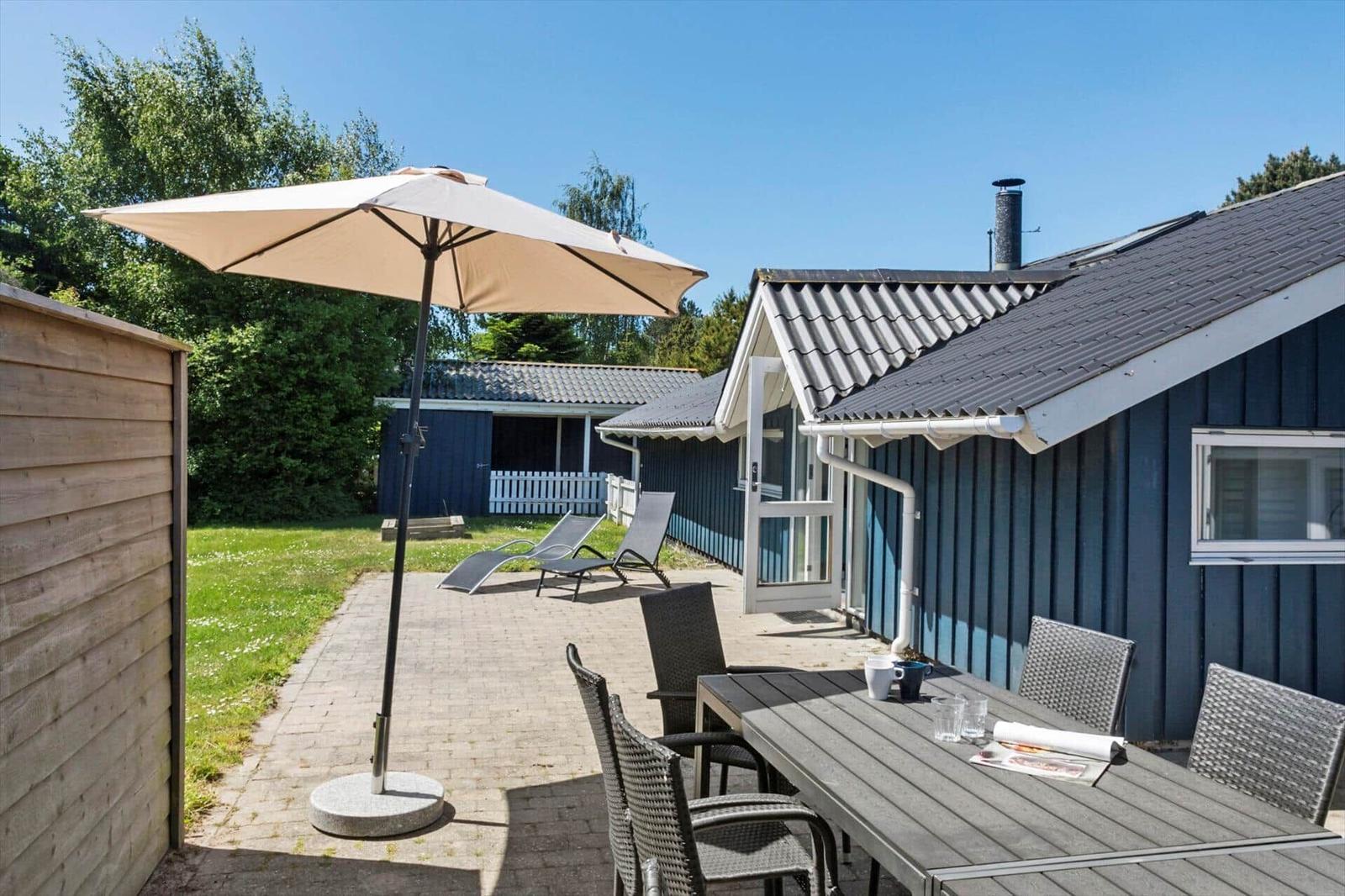 Terrasse mit Tisch, Stühlen und Sonnenschirm neben blauem Haus.