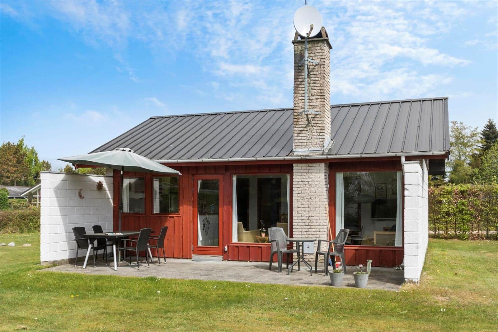 Ein Haus mit rotem Holz, grauem Dach und Terrasse mit Tisch und Stühlen.