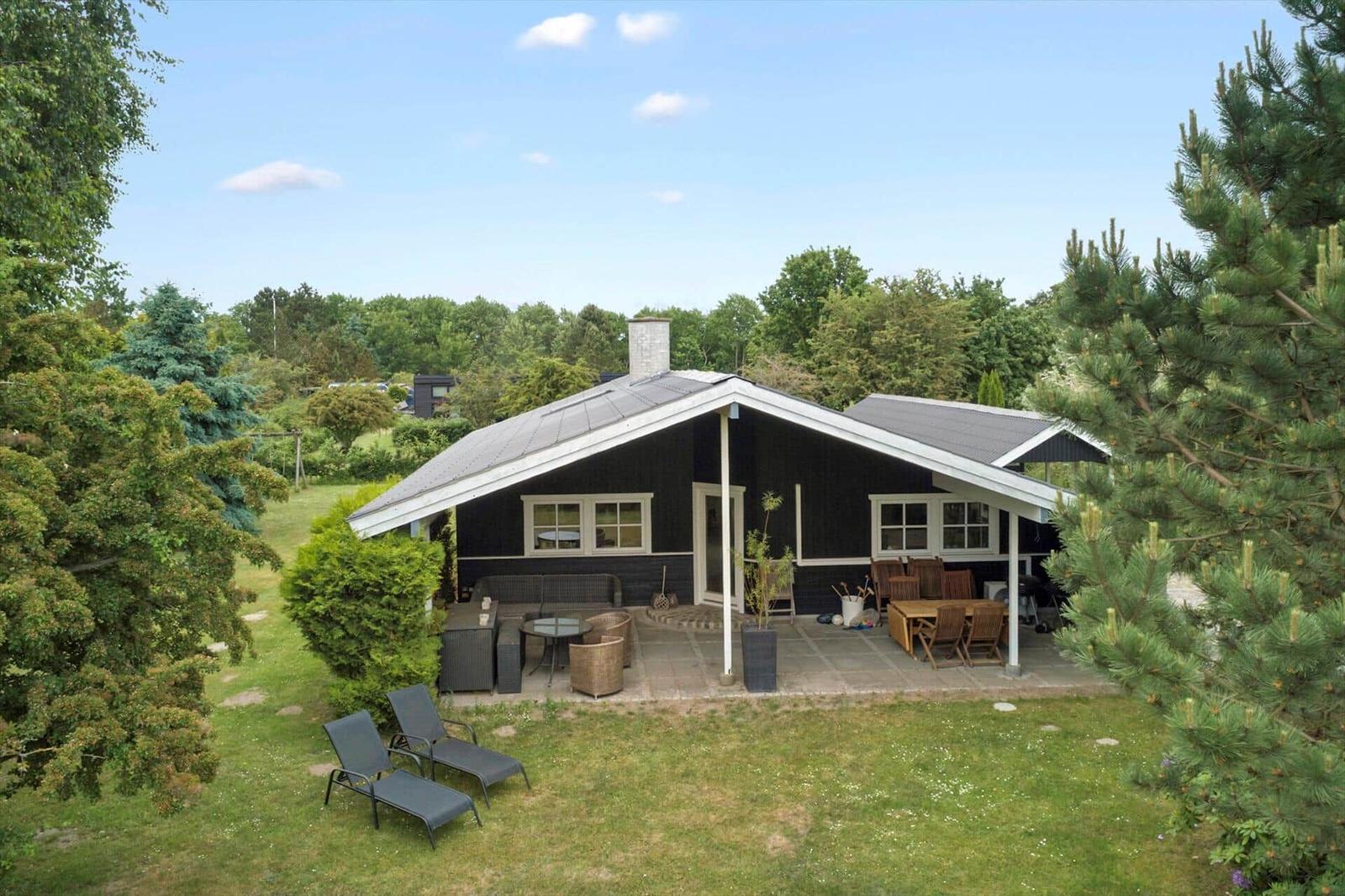 Schwarze Hütte mit Terrasse, Garten und Außensitzgelegenheiten.
