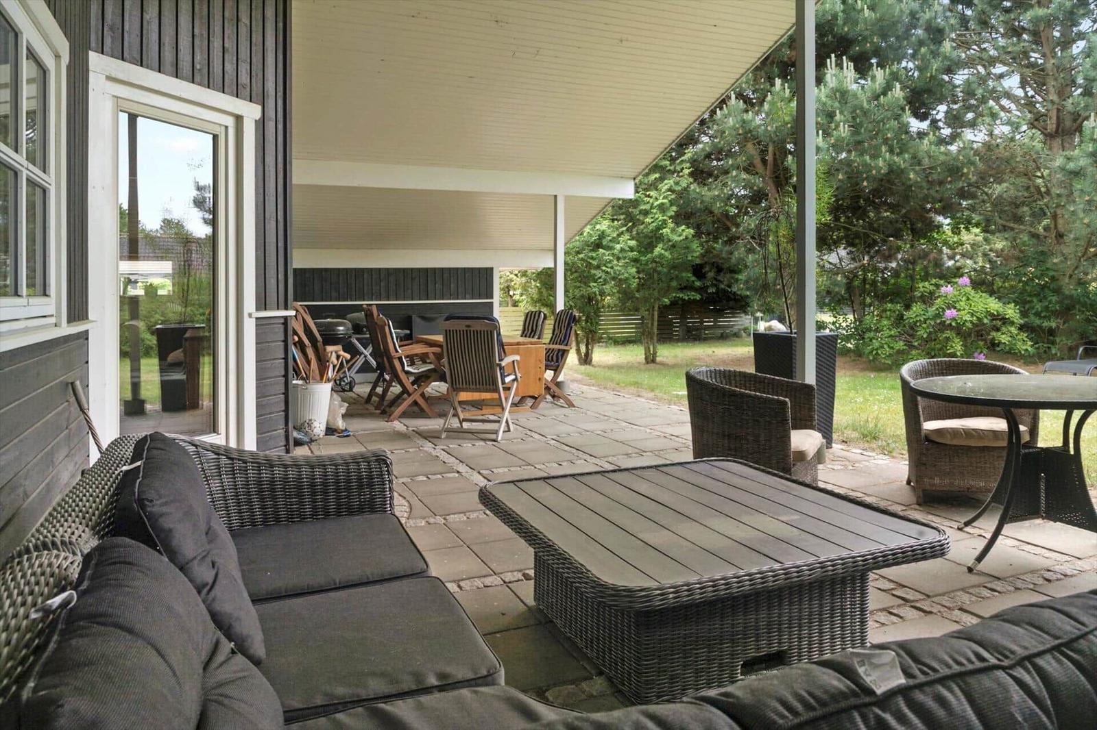 Terrasse mit Sitzgruppe, Tisch und Grillbereich unter Dach.