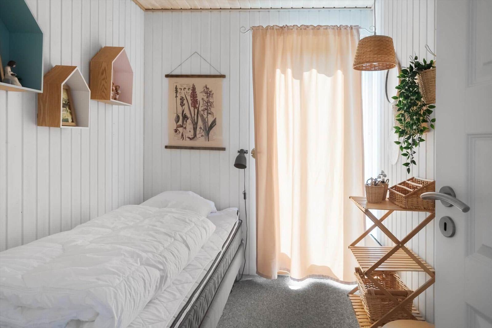 Ein Schlafzimmer mit Bett, Wandregalen und Vorhang vor Fenster.