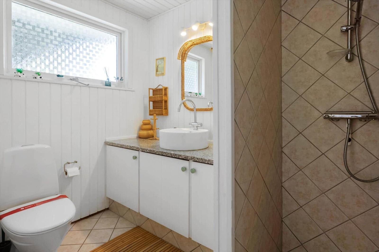 Badezimmer mit Toilette, Waschbecken und Dusche. Weiße Wände und beigefarbene Fliesen.
