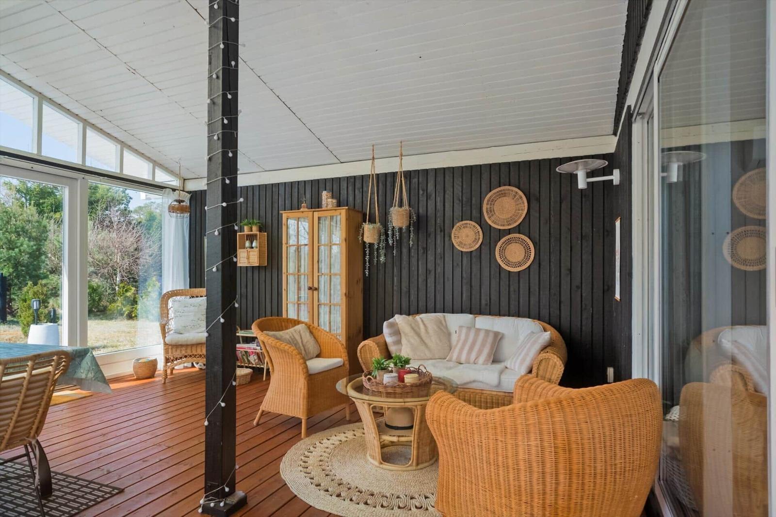 Terrasse mit Rattanmöbeln, dunkler Holzwand und hängenden Pflanzen.