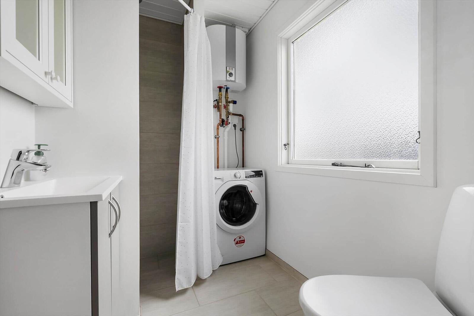 Badezimmer mit Waschmaschine, Dusche und Toilette. Fenster mit getöntem Glas.