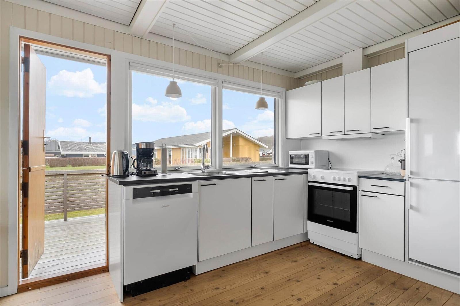 Küche mit weißen Schränken, Holzboden und Blick auf Balkon und Garten.