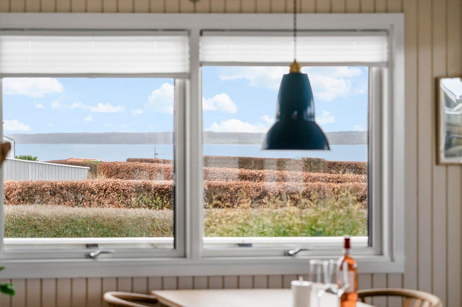 Durch das Fenster sieht man einen See und einen Heckenbereich.