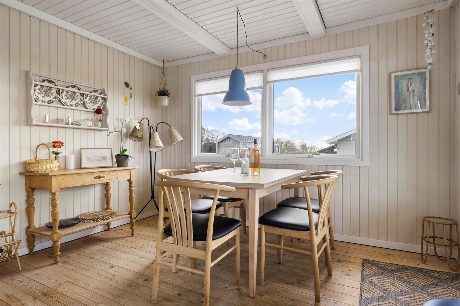 Essbereich mit Holztisch, Stühlen und großem Fenster. Wandregale und Holzboden.