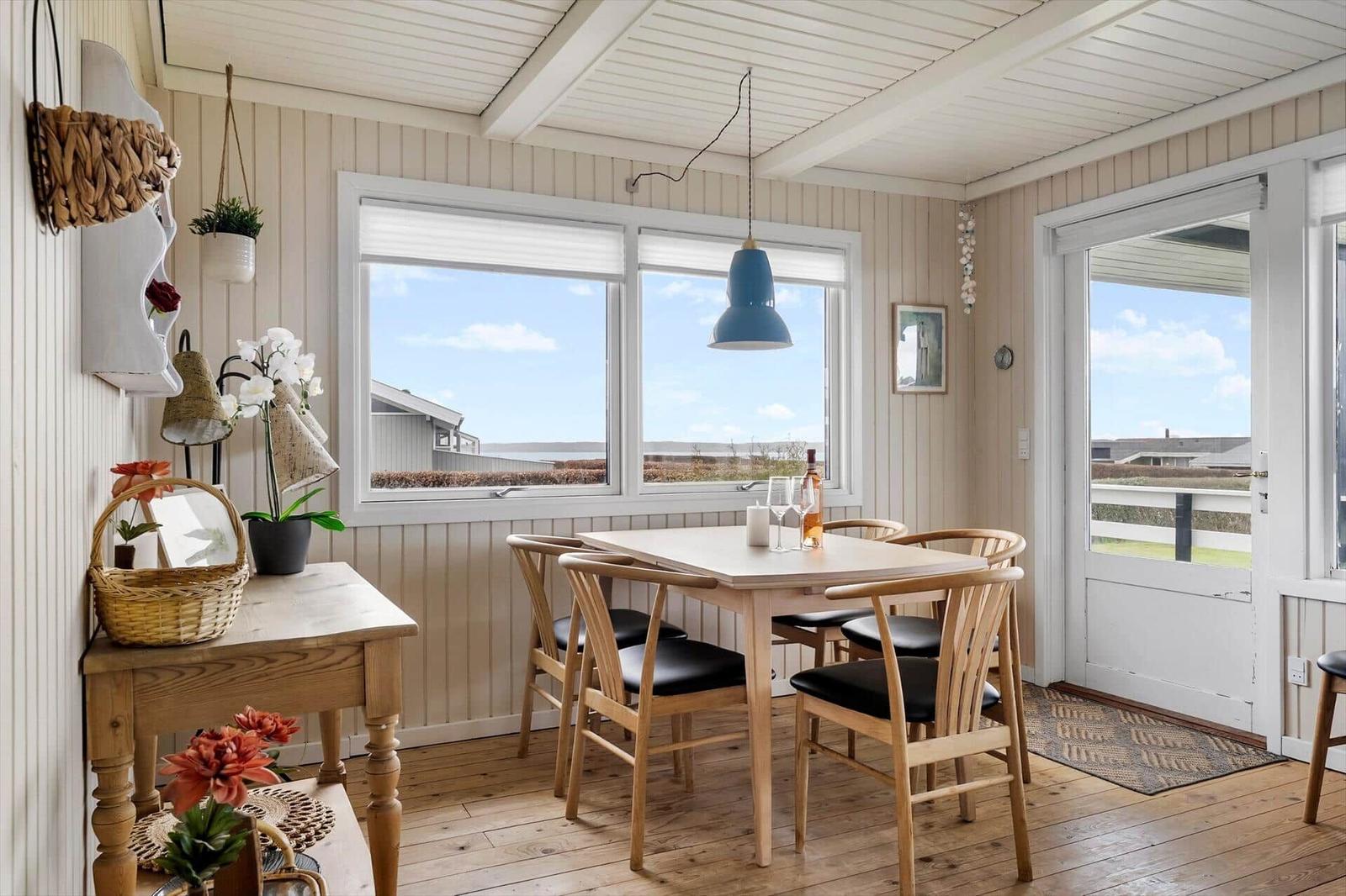 Esszimmer mit Holztisch, Stühlen und Fensterblick auf Landschaft.