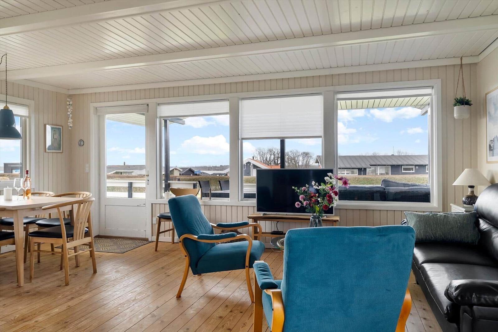 Wohn- und Essbereich mit blauen Sesseln, Fernseher und Blick auf die Terrasse.