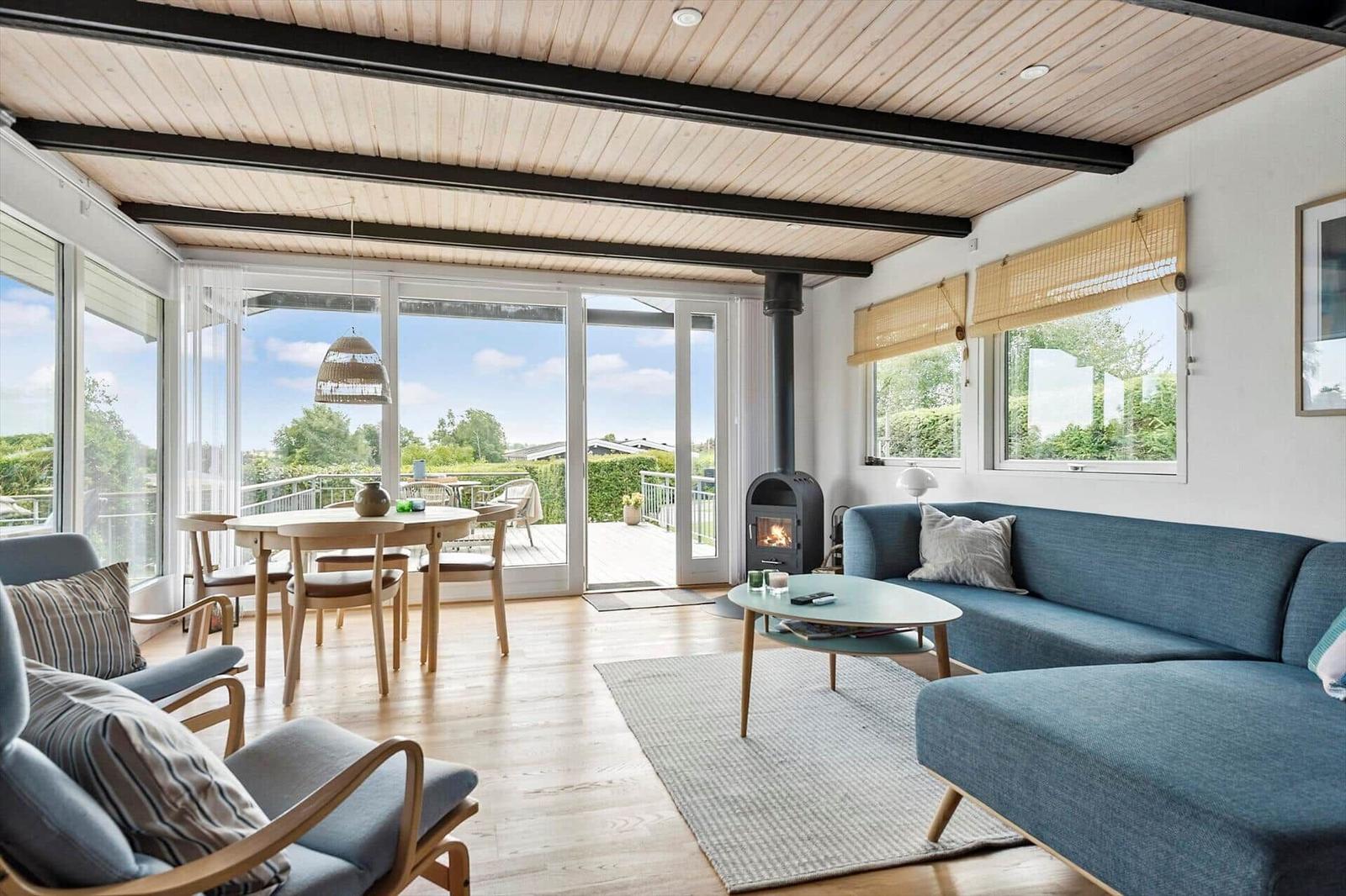 Wohn- und Essbereich mit Sofa, Tisch und Kamin. Große Fenster und Terrasse.