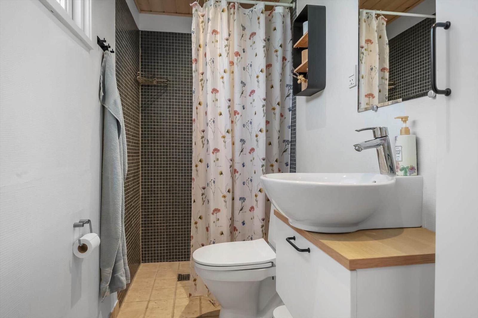 Badezimmer mit Dusche, Waschbecken und Toilette. Duschvorhang mit Blumenmuster.
