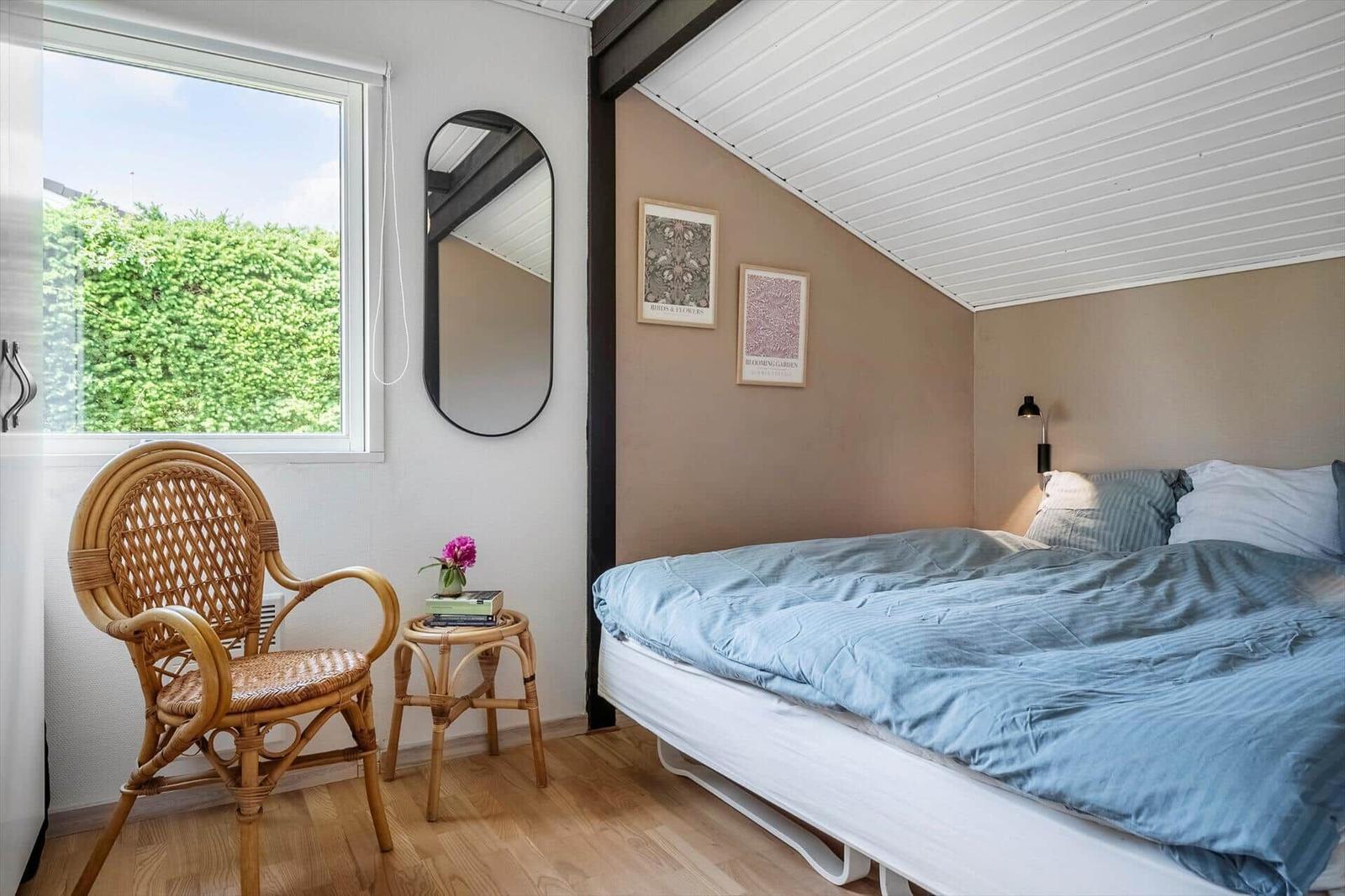 Schlafzimmer mit Bett, Stuhl und Fenster zum Grün.