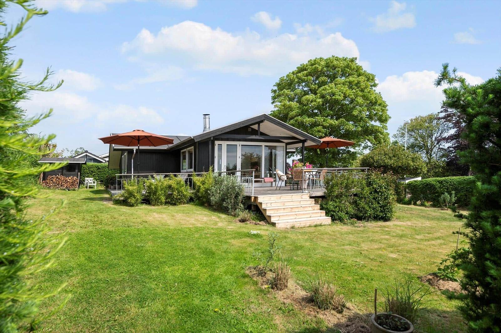 Moderne Holzhütte mit Terrasse, Garten und Sonnenschirmen. Blick auf grünen Rasen und Bäume.