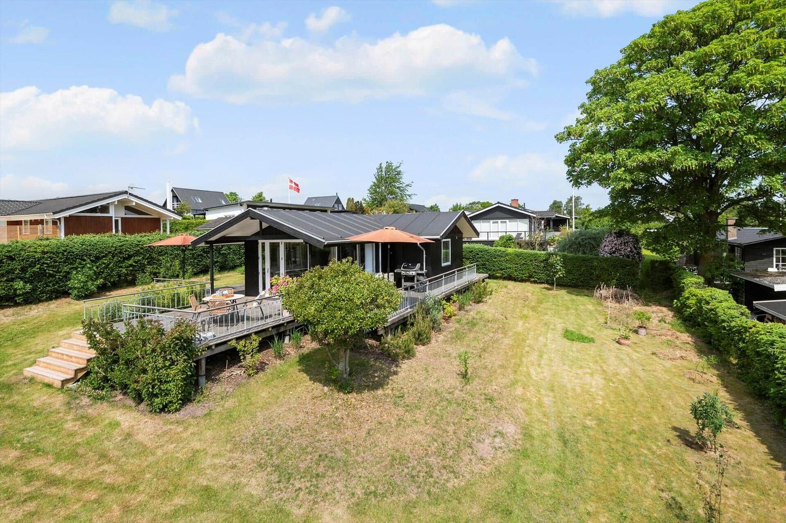 Ein Haus mit Terrasse, Grill und Garten unter blauem Himmel.