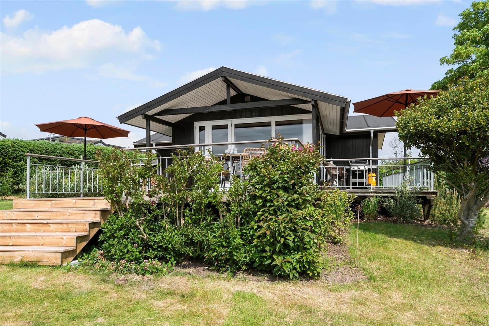 Moderne Holzhütte mit Balkon, Garten und Sonnenschirmen.