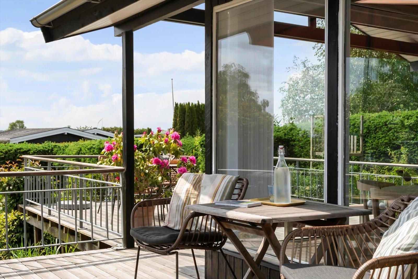 Terrasse mit Tisch, Stühlen und Blumen. Blick auf grünen Garten und Himmel.