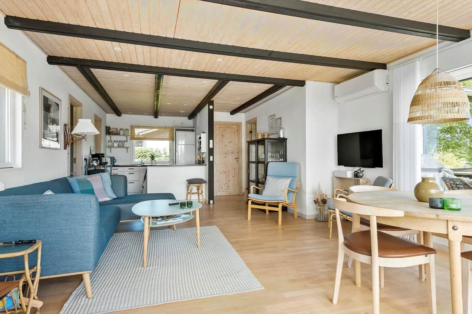 Wohn- und Essbereich mit Holzdecke, Sofa, Tisch und Fernseher.