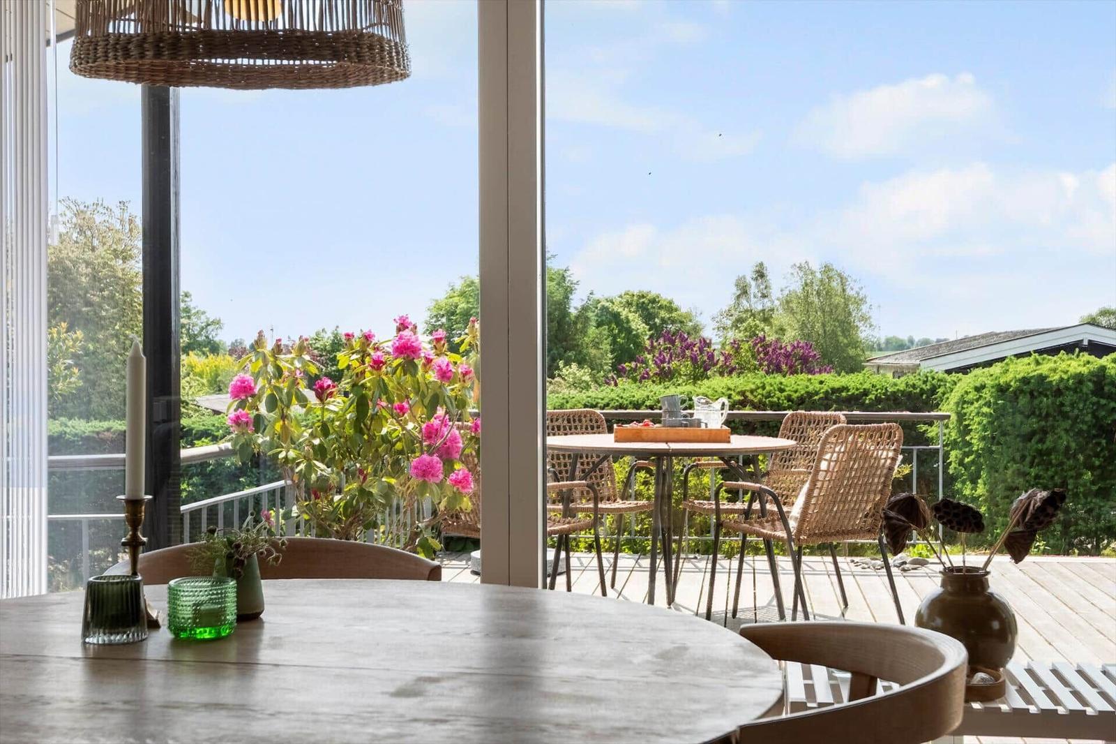 Terrasse mit Tisch und Stühlen, Blick auf grüne Bäume und Blumen.