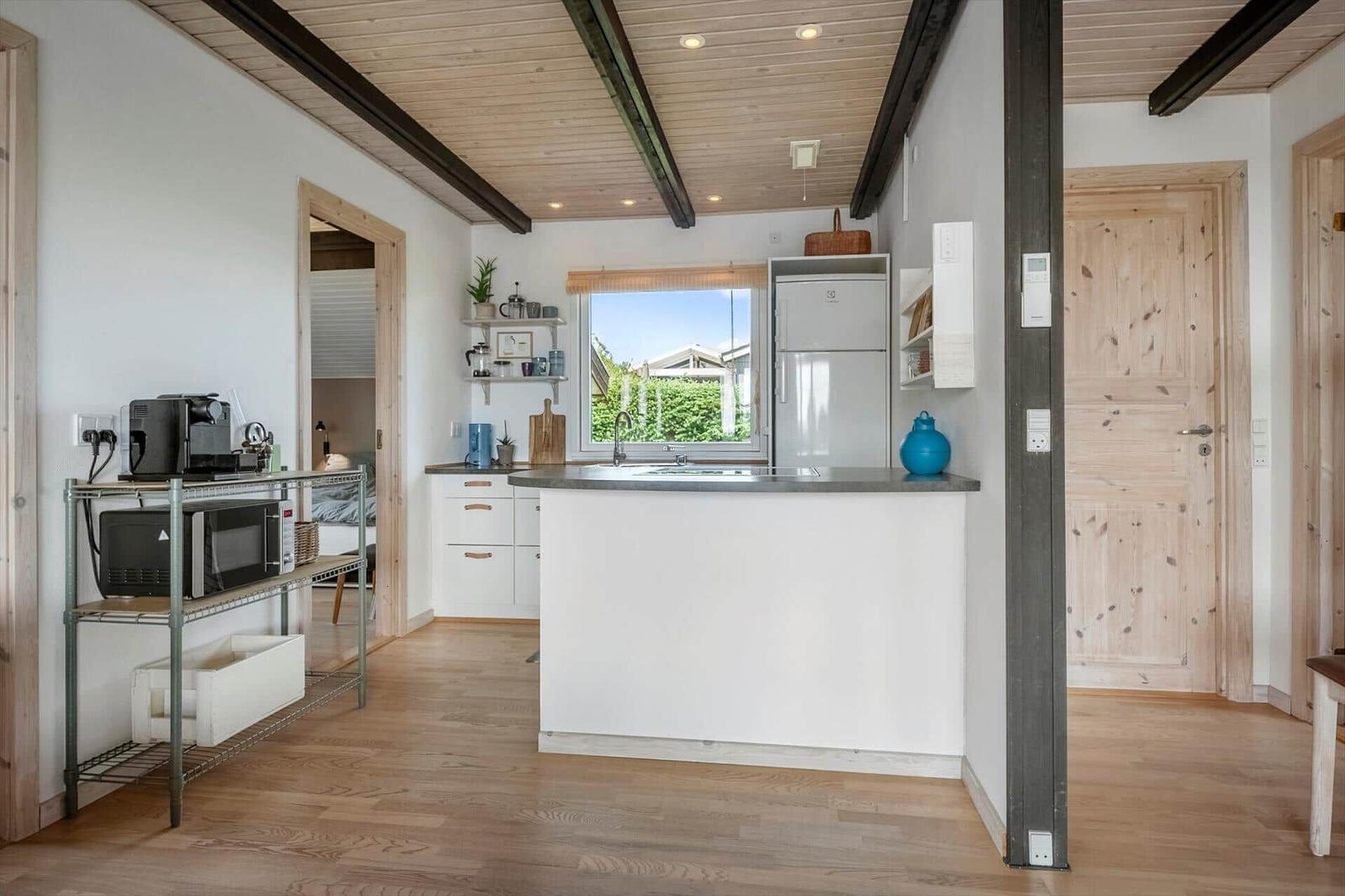 Küche mit Arbeitsplatte, Kühlschrank und Fenster. Holzfußboden und Deckenbalken.