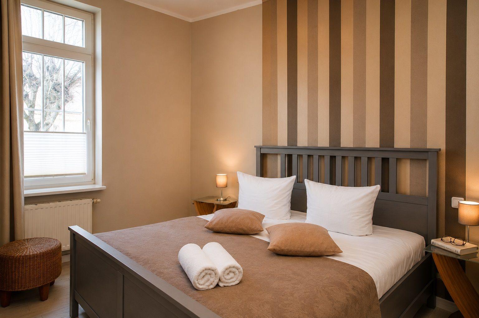 Ein Schlafzimmer mit Bett, Nachttischen und Fenster. Wand mit Streifenmuster.