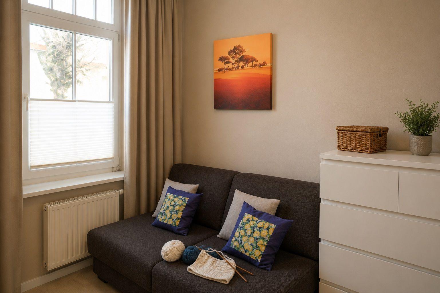 Ein dunkler Sofa mit Kissen, Wandbild und Fenster mit Jalousie.