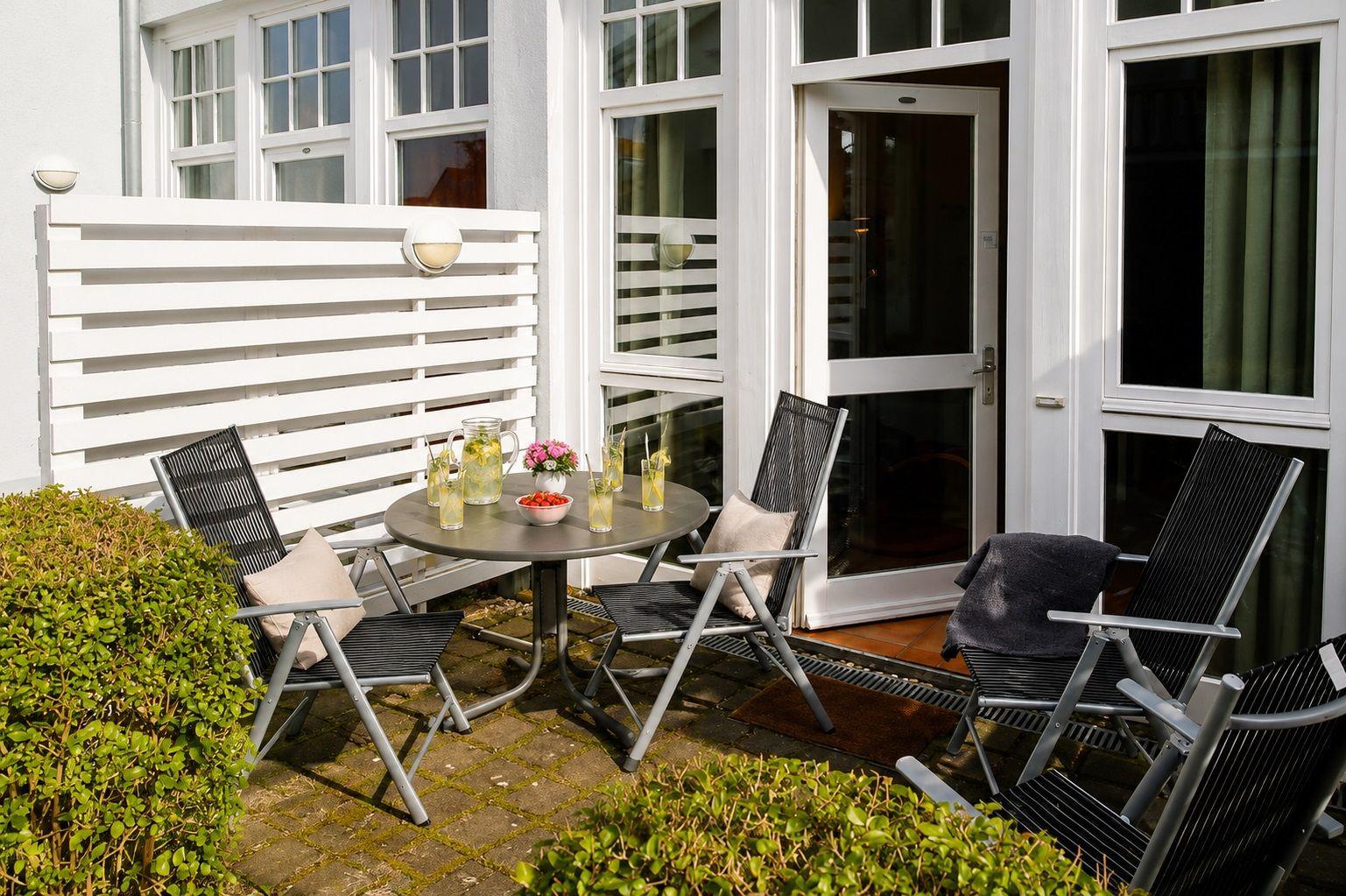 Terrasse mit Tisch, Stühlen und Blumen vor einer weißen Hauswand.