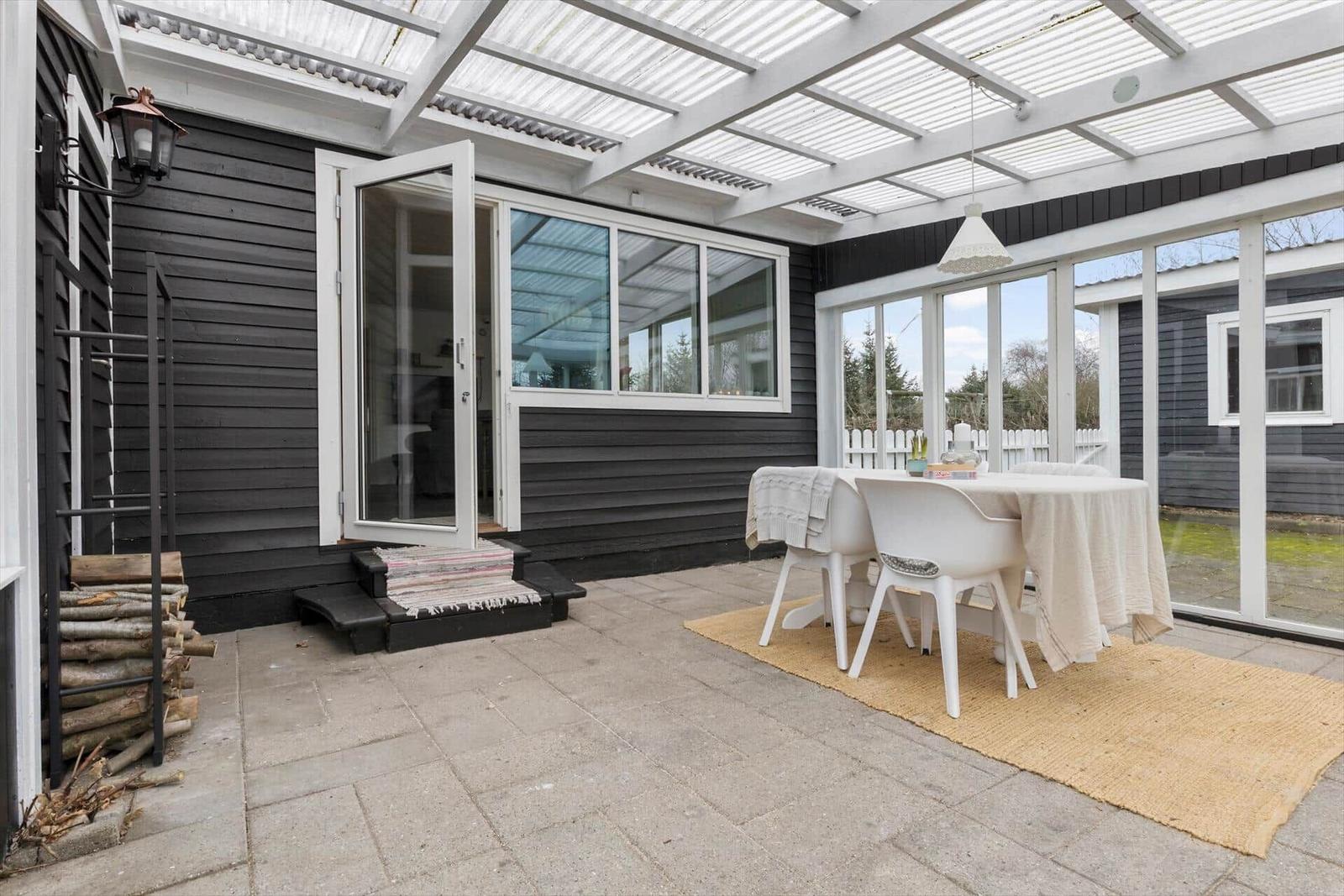 Außenbereich mit Tisch, Stühlen und Grill neben einem Haus mit weißen Fenstern.