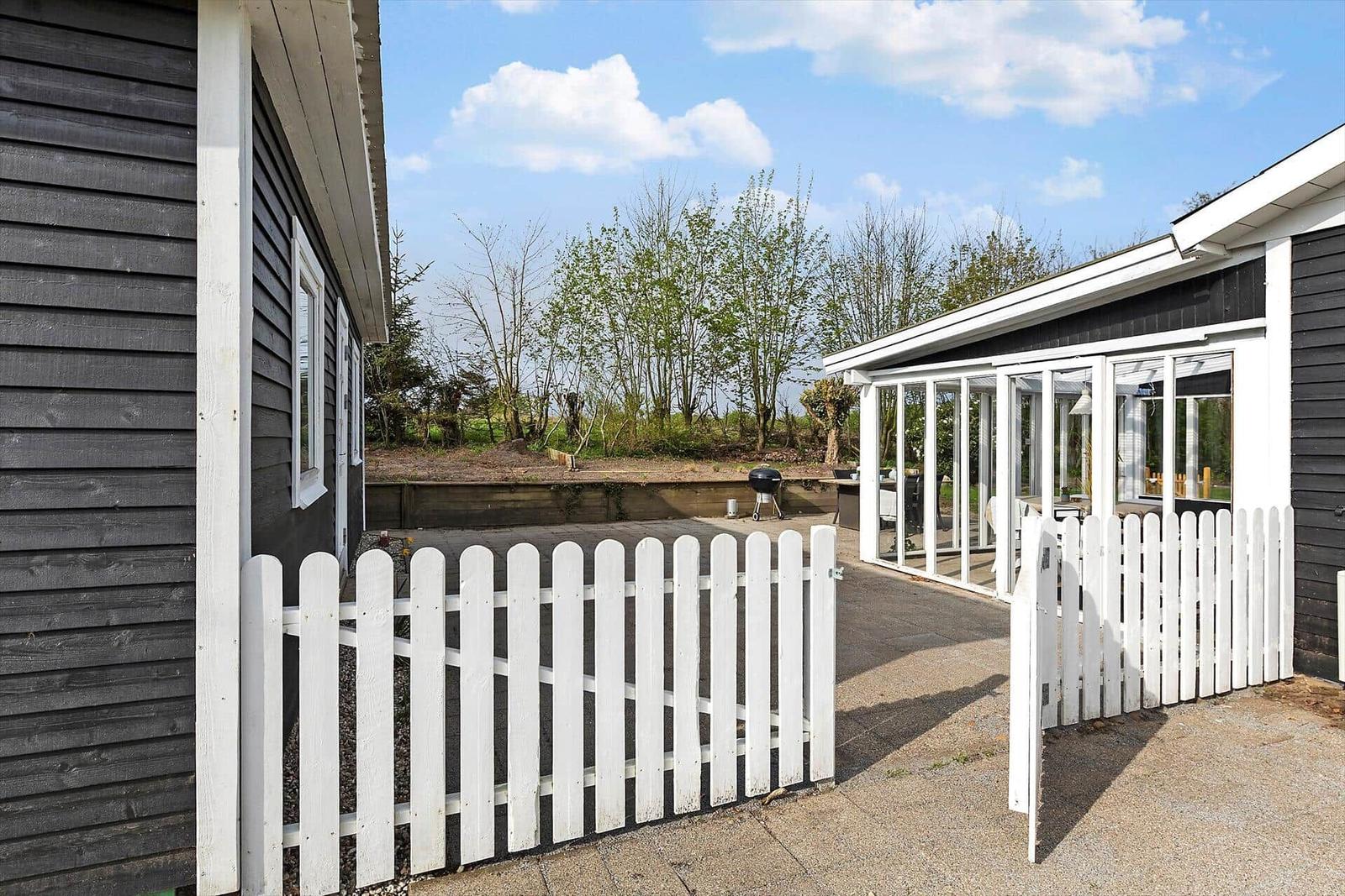 Terrasse mit Grill, Tisch und Sitzgelegenheiten neben einem Haus mit Glasveranda.
