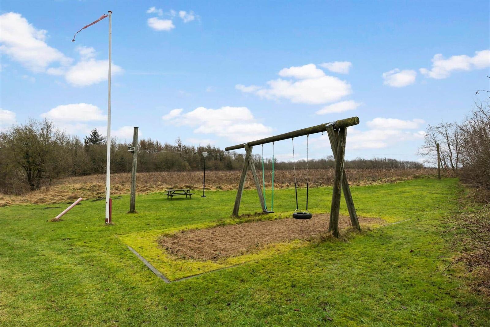 Grünes Feld mit Schaukel und Picknicktisch unter blauem Himmel.
