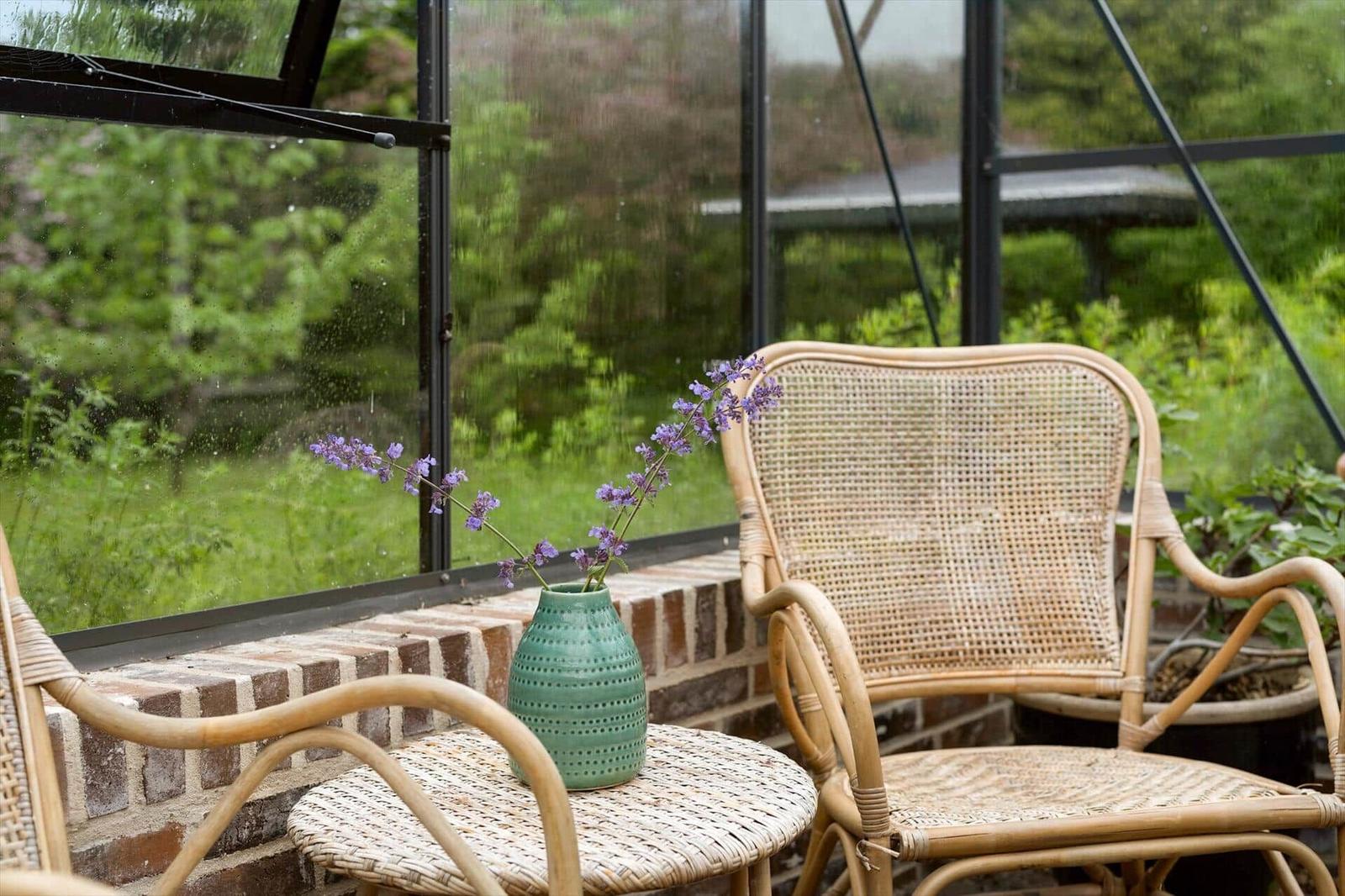 Rattan-Stuhl und Tisch mit Vasenblumen vor Glaswand