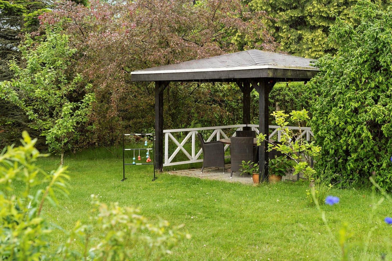Gartenhütte mit Tisch und Stühlen, umgeben von Gras und Bäumen.
