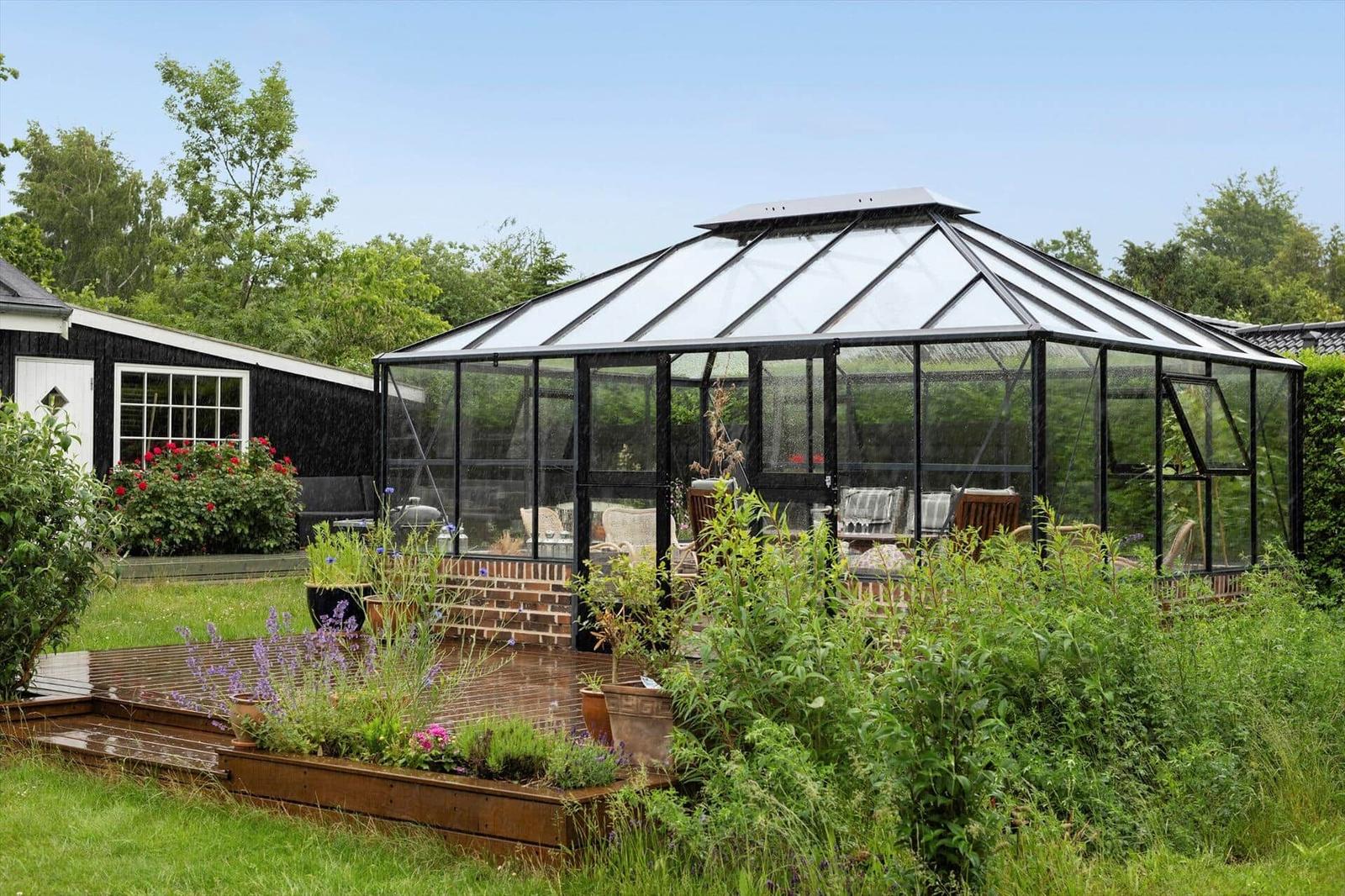 Gartenhaus mit Glasdach und Sitzgelegenheiten im Garten.
