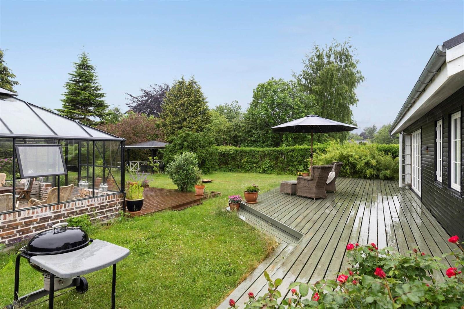 Hinterhof mit Terrasse, Grill und Glasveranda. Umgeben von Grün und Bäumen.